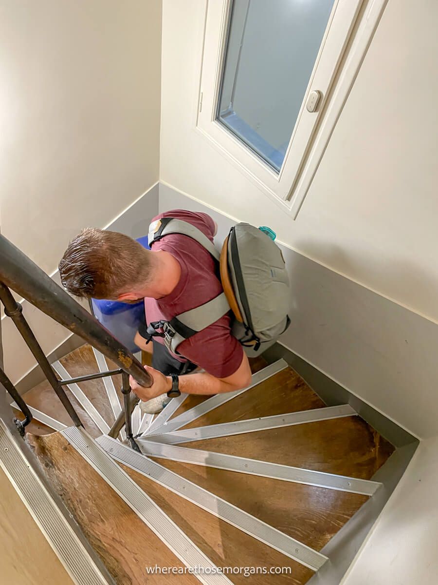 Man carrying a large suitcase down a narrow stairway in Europe