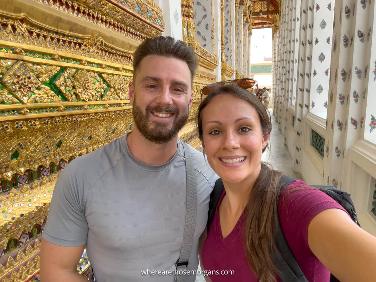 Mark and Kristen Morgan from Where Are Those Morgans stood next to each other taking a selfie inside a palace in Bangkok Thailand