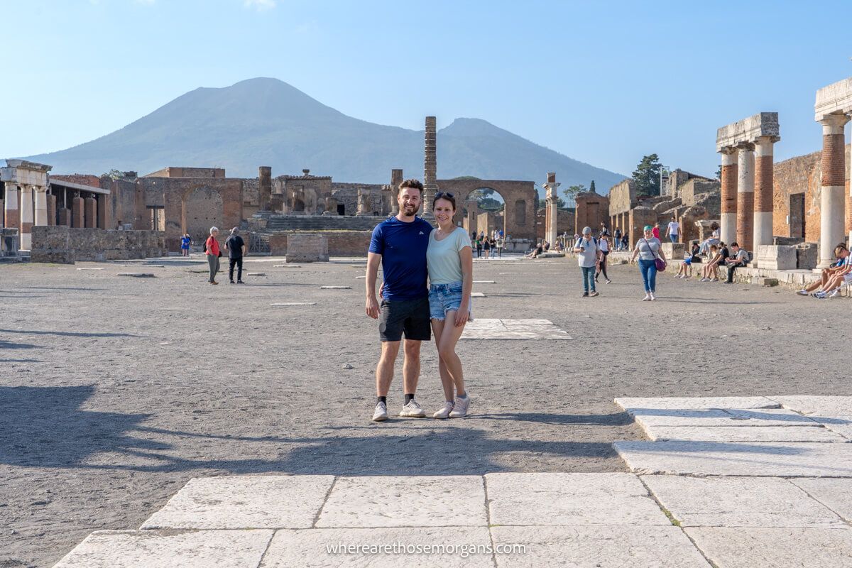 Couple standing together for a photo in Pompeii main square with ruins and a volcano behind