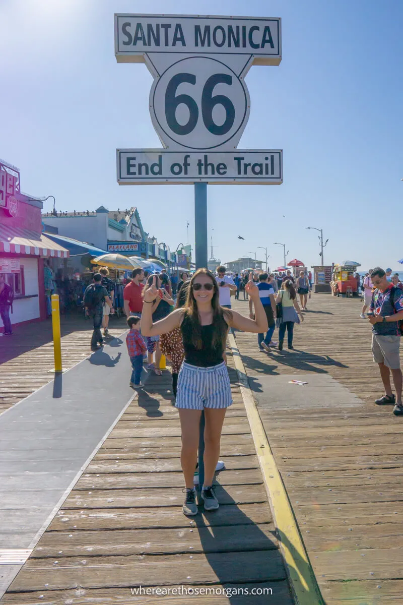 Woman standing under the end of Route 66 trail sign on the Santa Monica Pier in Los Angeles