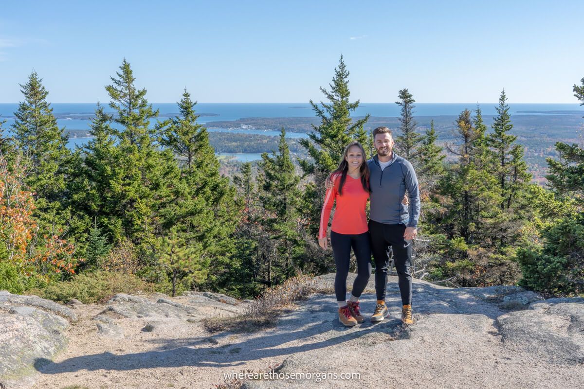 A couple of people taking a photo at the summit of a hiking trail in Acadia, Maine