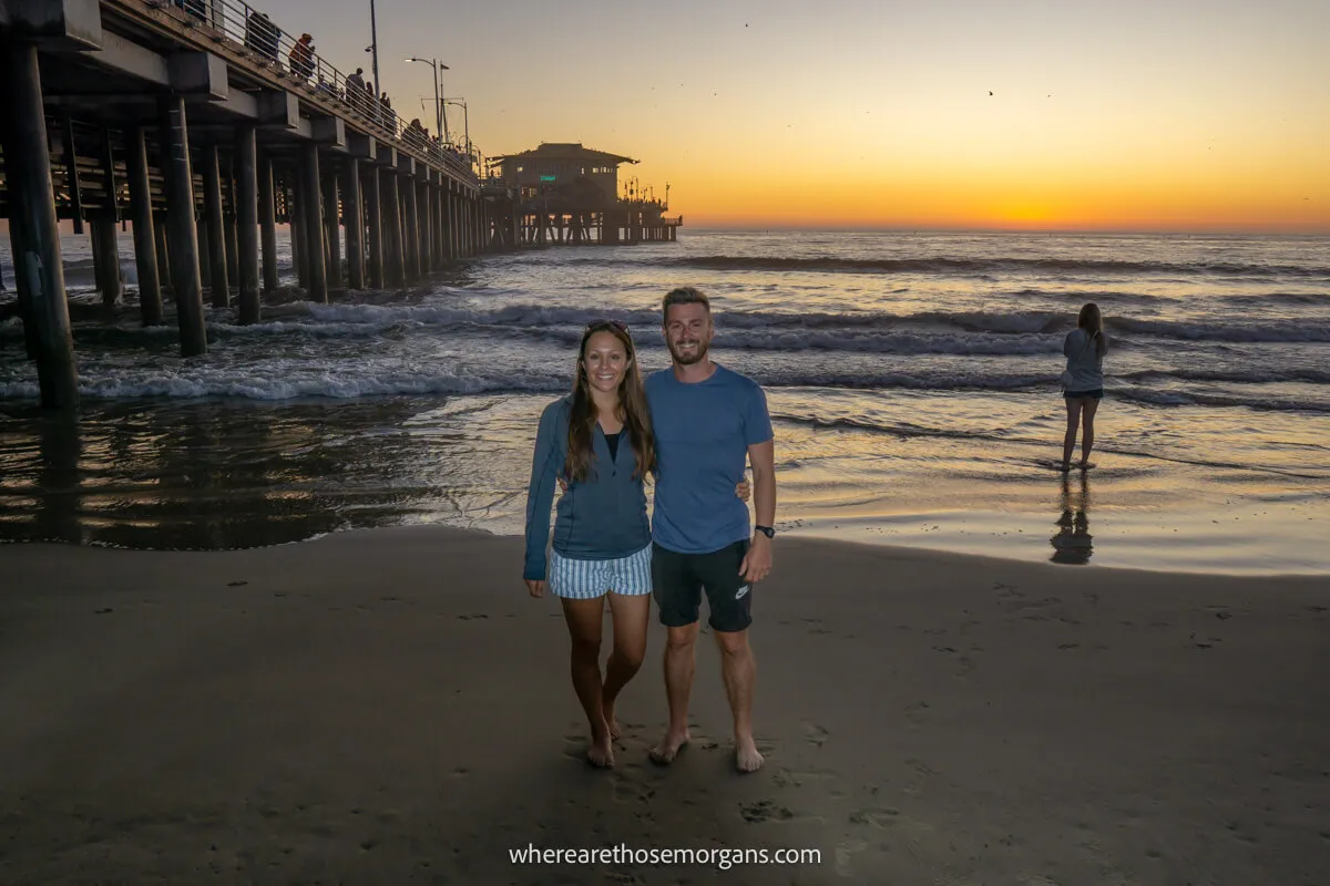 A couple posing for a photograph during sunset on the Santa Monica Beach underneath the Pier