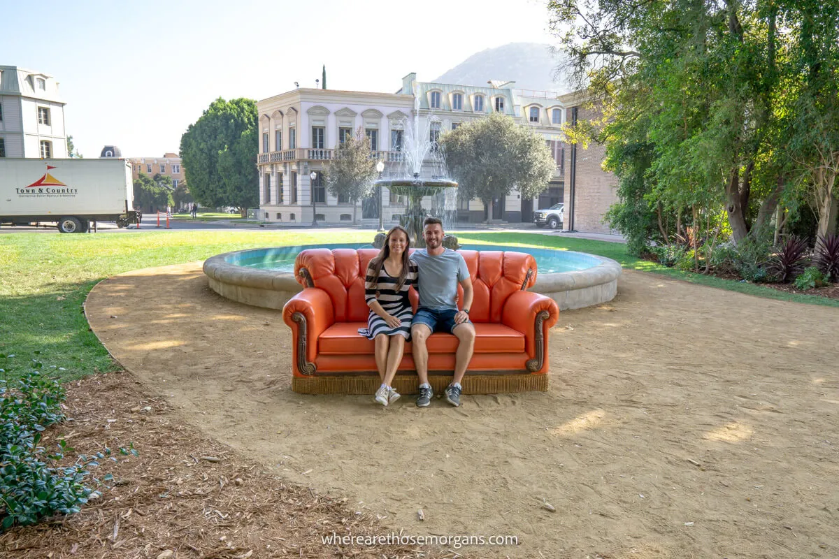 A man and woman sitting on the bright orange couch from Friends on a movie set