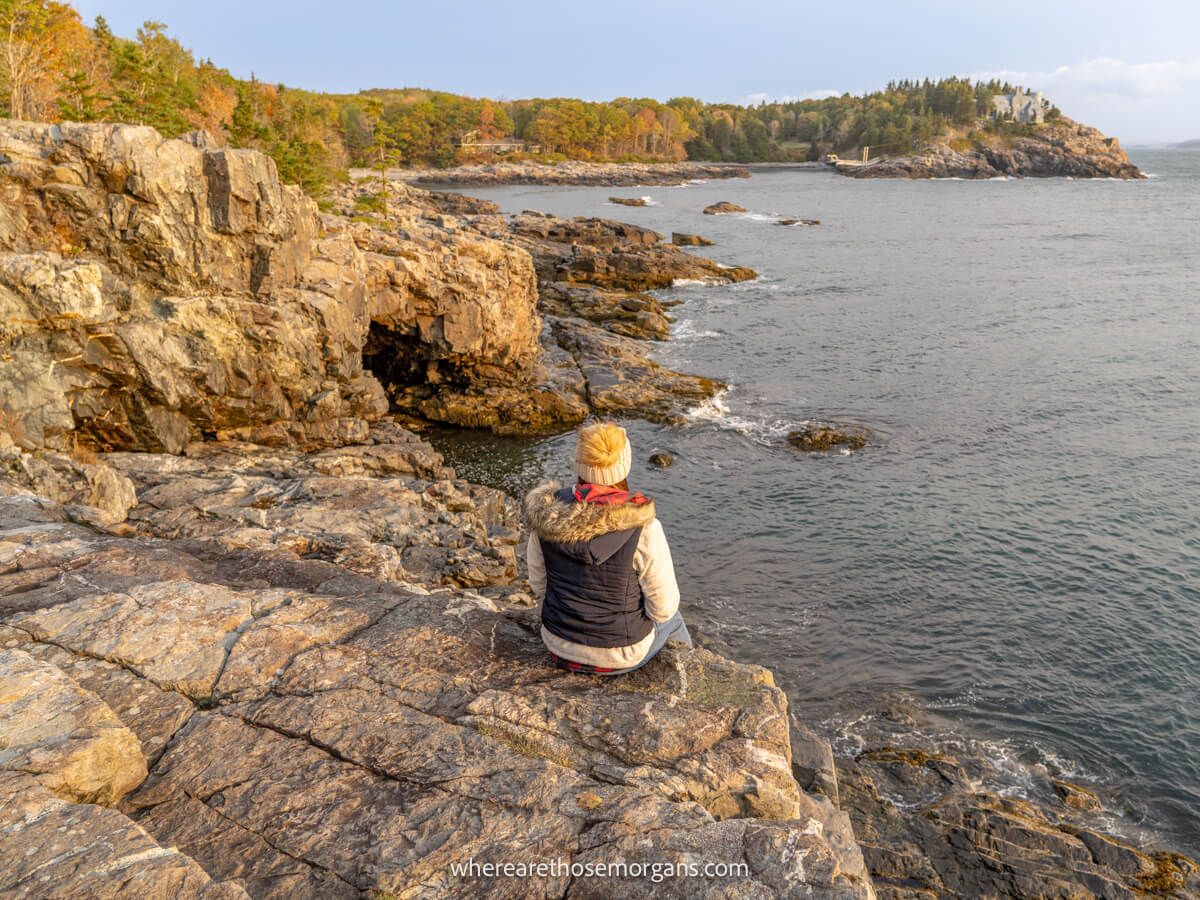 Person sitting on a rocky cliff edge overlooking the views of the coast and the ocean in Acadia National Park