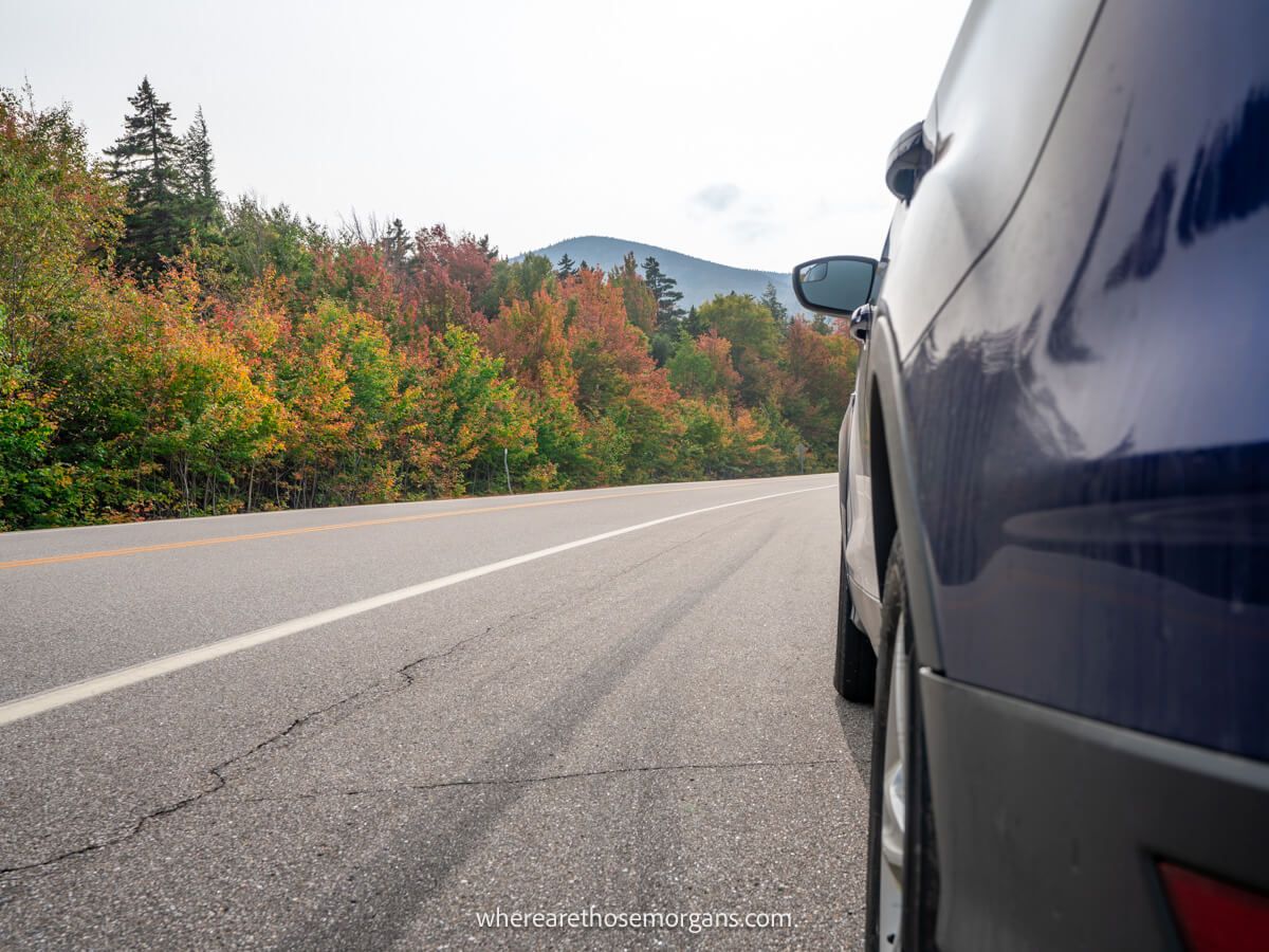 Close up of the back side of a car on a road with trees and hills