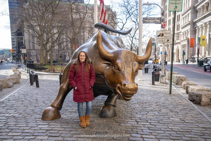 Tourist in red coat standing next to a large bronze bull statue in a city