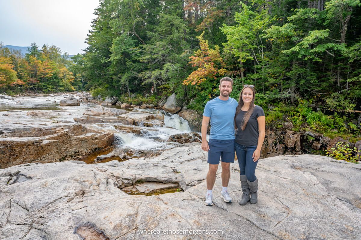 Couple standing together for a photo on a rocky surface with trees and a river behind