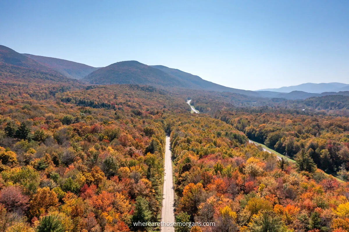 Drone photo from high up looking down at two roads cutting through an ocean of colorful trees in the autumn