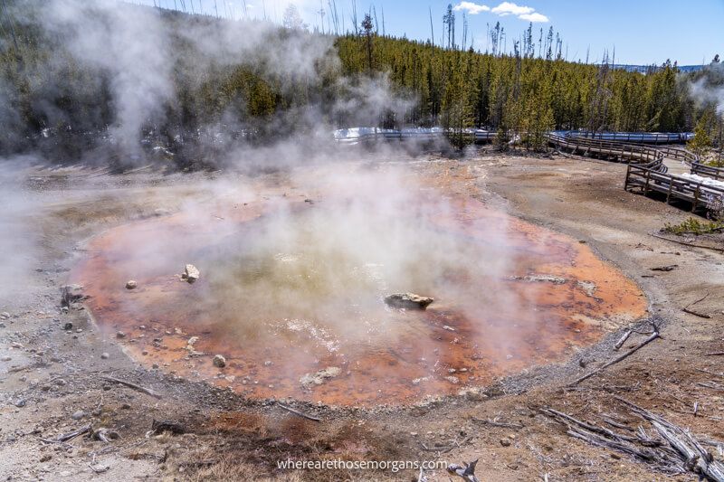 Round red colored hot spring in a charred field with light steam venting