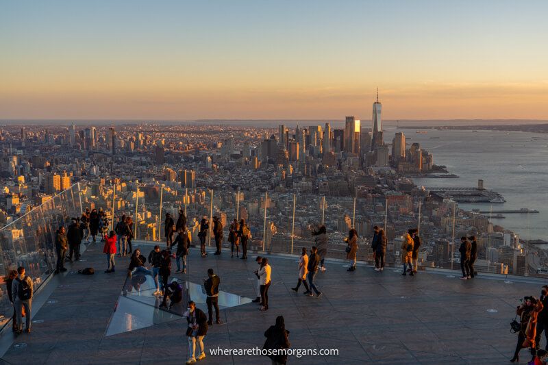 The sunset view over an outdoor observation deck and Downtown NYC with soft yellows in the sky