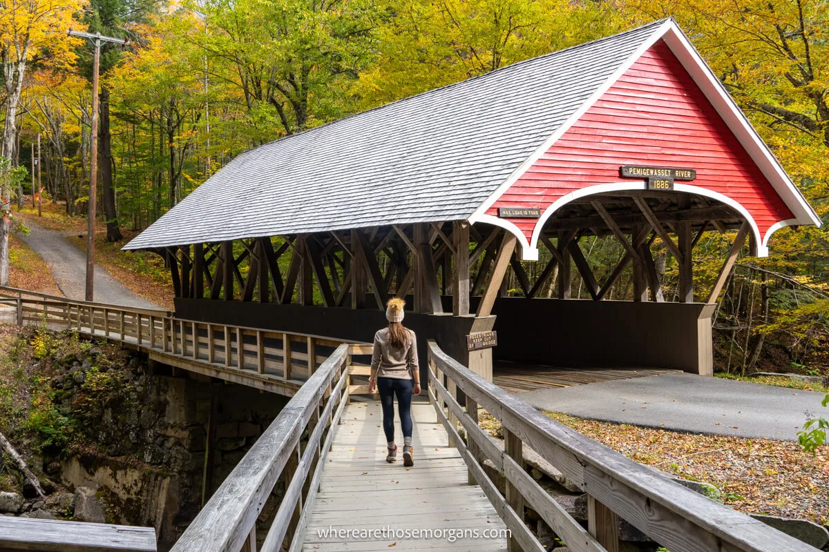 Tourist in hat walking across a wooden path to a wooden covered bridge on a New England fall road trip