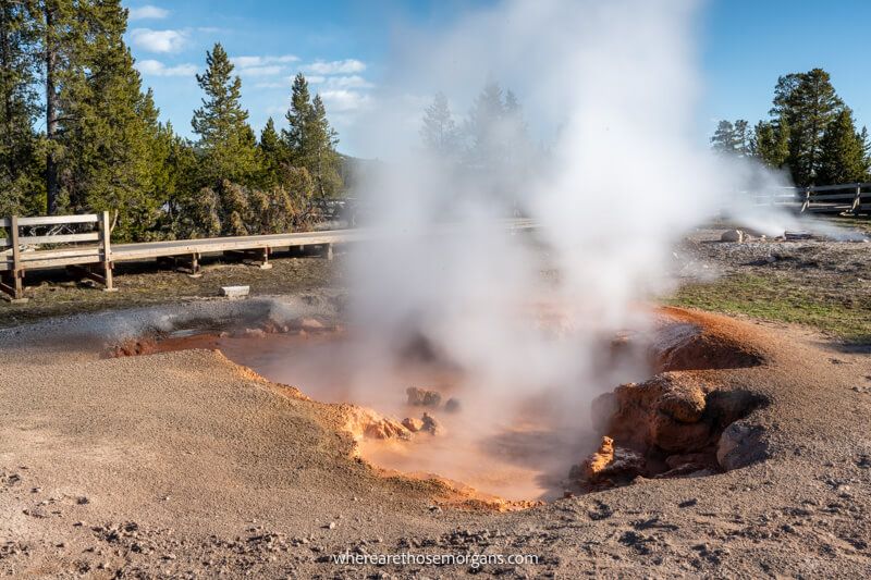 Orange and brown dirt with steam venting near a wooden boardwalk