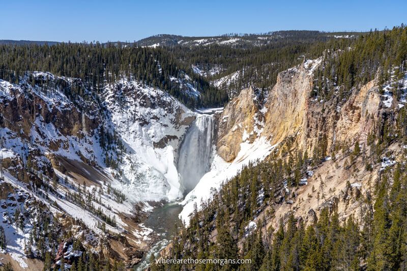 Canyon view with a powerful waterfall at the back surrounded by trees and snow