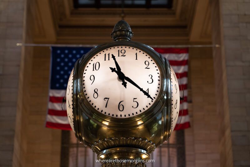 Close up of a four sided clock in Grand Central Terminal in NYC with an American flag flying behind