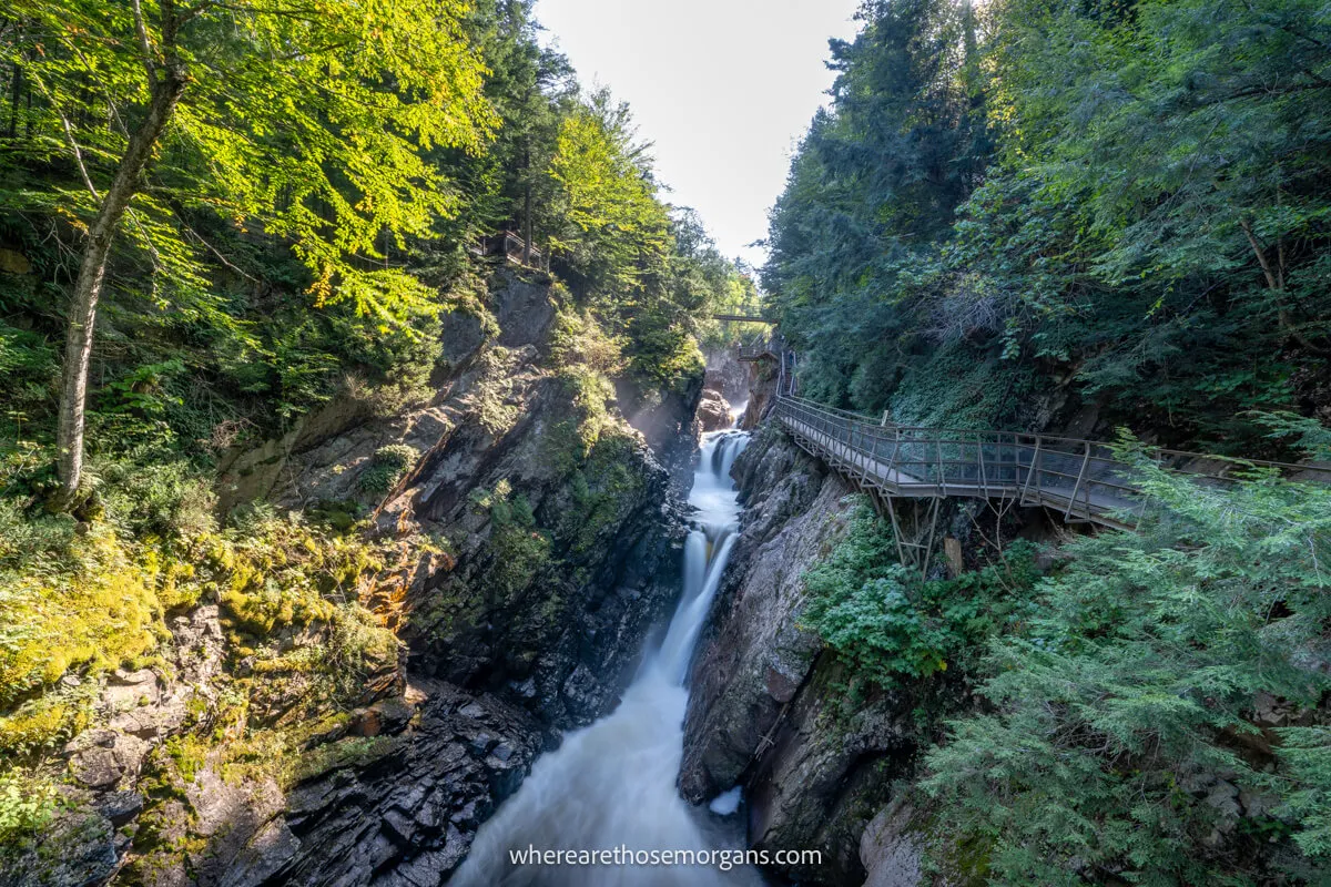 Waterfall cutting through a narrow gorge with a wooden walkway to the side and lots of trees on both banks