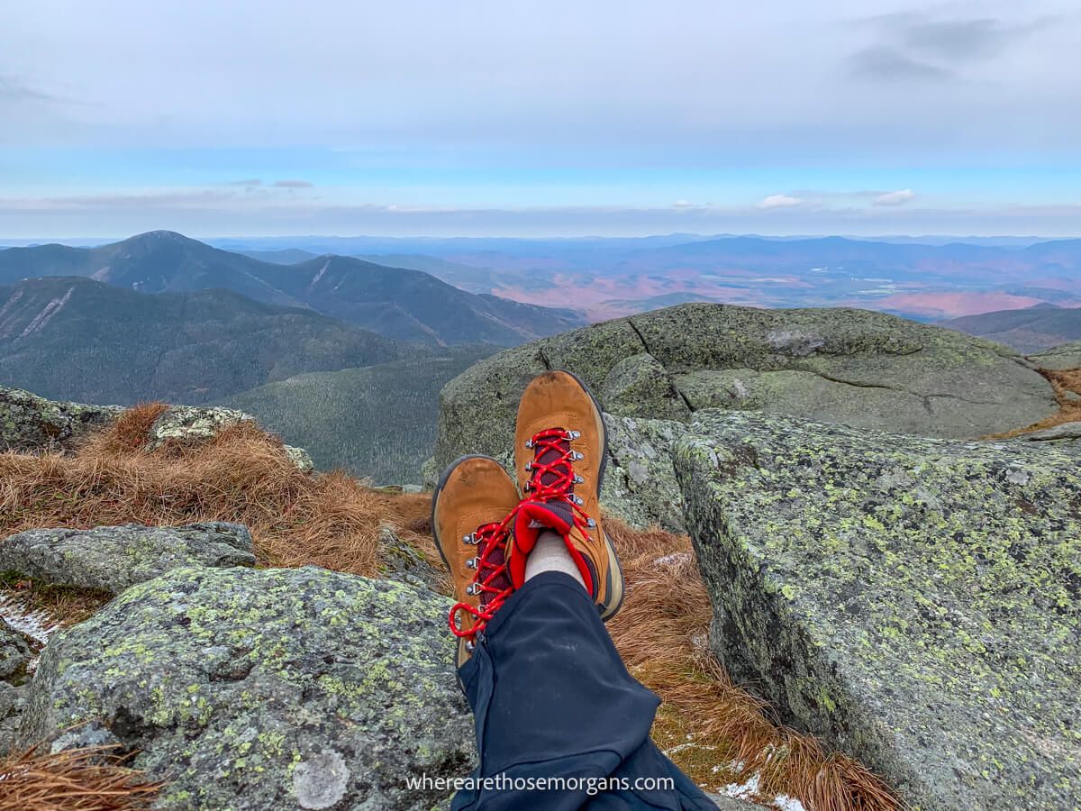 Legs and hiking boots on rocks with distant views on a cloudy day from a mountain summit