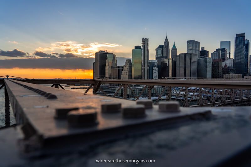 Sunset view of a steel beam on Brooklyn Bridge overlooking Lower Manhattan skyline with skyscrapers