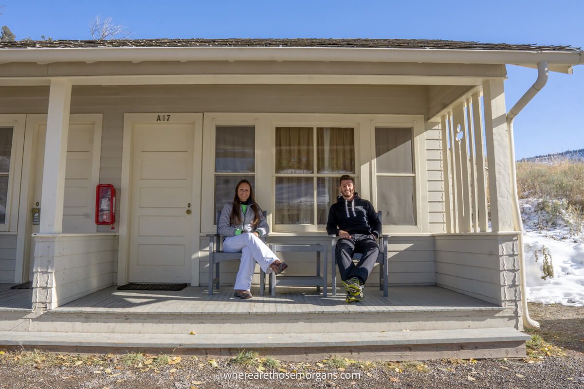 Couple sat together at a table on a porch outside a wooden cabin on a clear sunny day in Yellowstone National Park