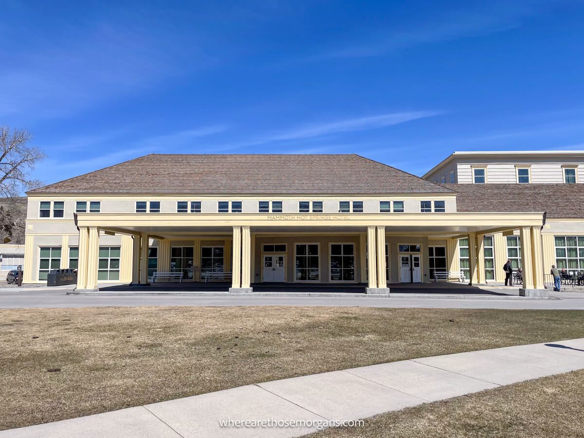 Exterior photo of a hotel in Mammoth Hot Springs with two buildings and a covered porch behind a path under a clear blue sky