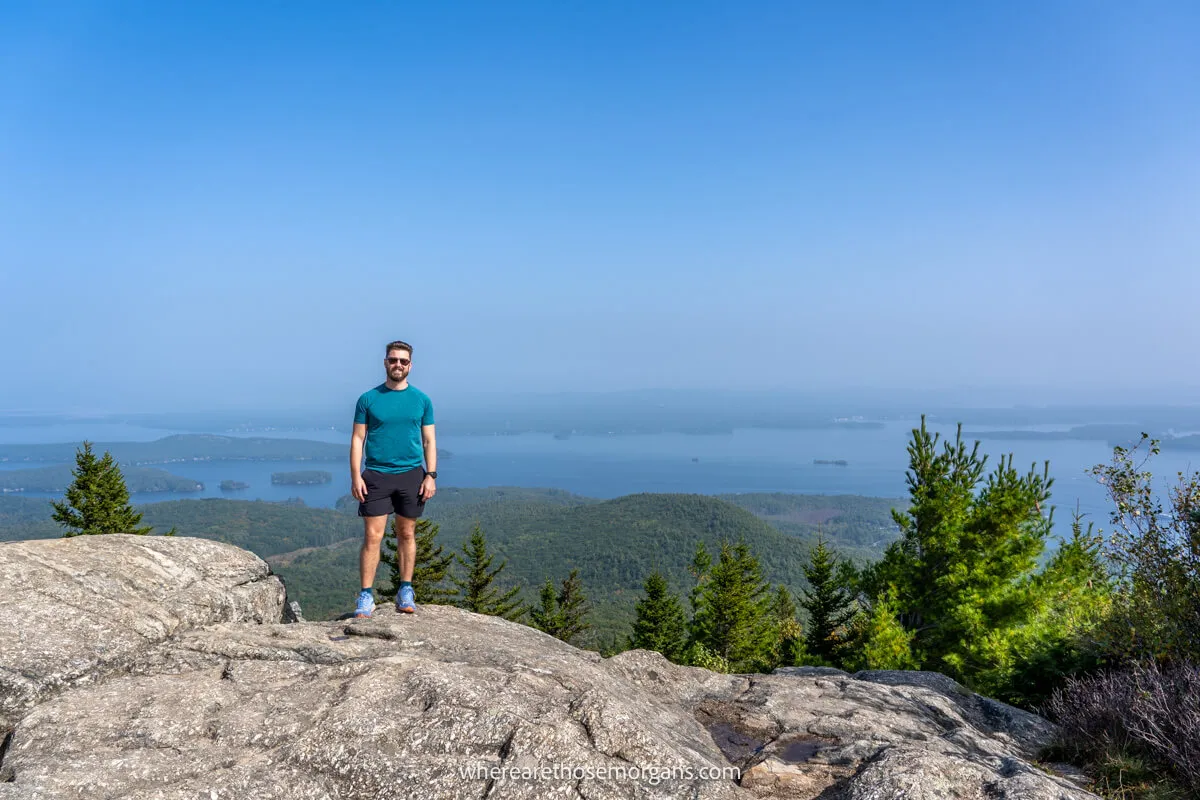 Hiker on a rocky summit with far reaching views over a large lake on a sunny day