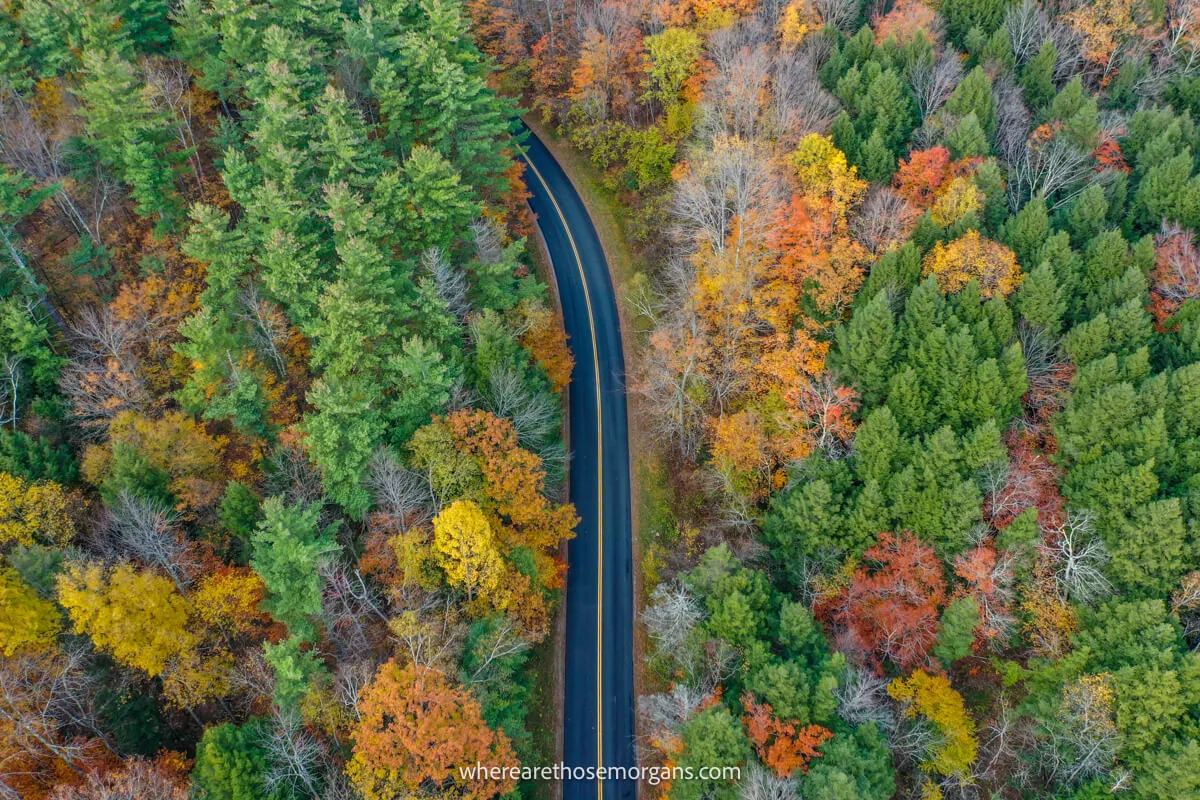 Drone photo looking down over a road in New England cutting through a forest in fall with colorful leaves