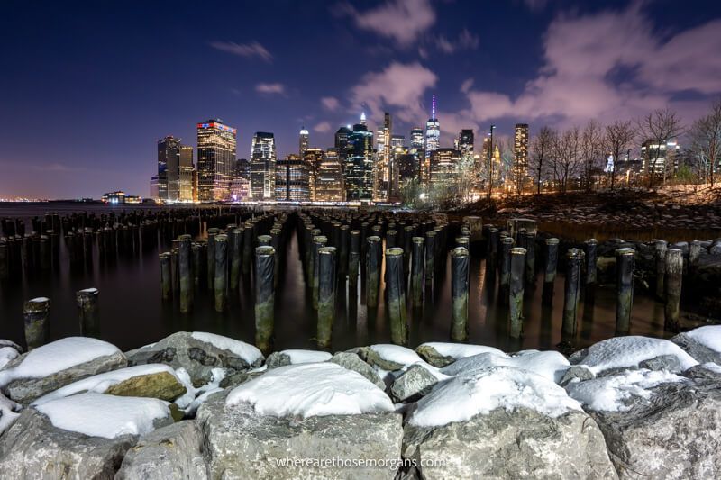 The NYC skyline from an old pier with wooden beams and snow on a wall at sunset