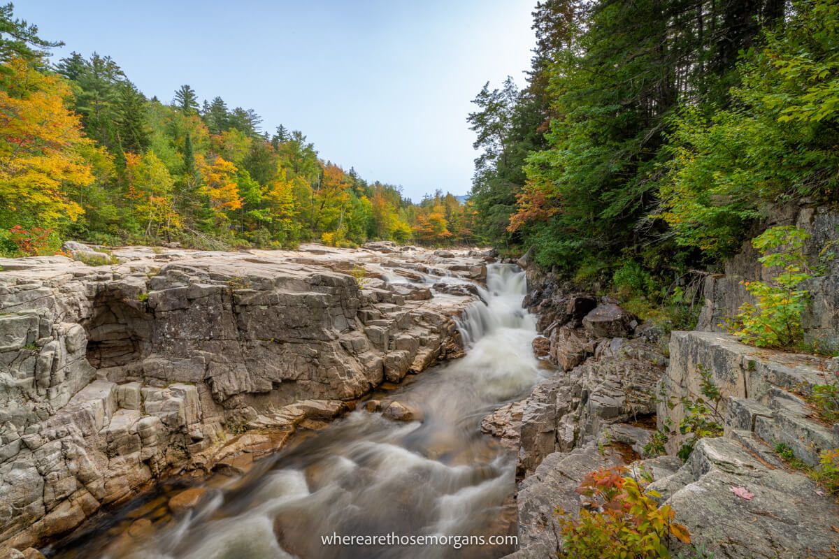 River running through a gorge with large rocks and boulders flanked by trees with colorful leaves on the Kancamagus Highway in fall