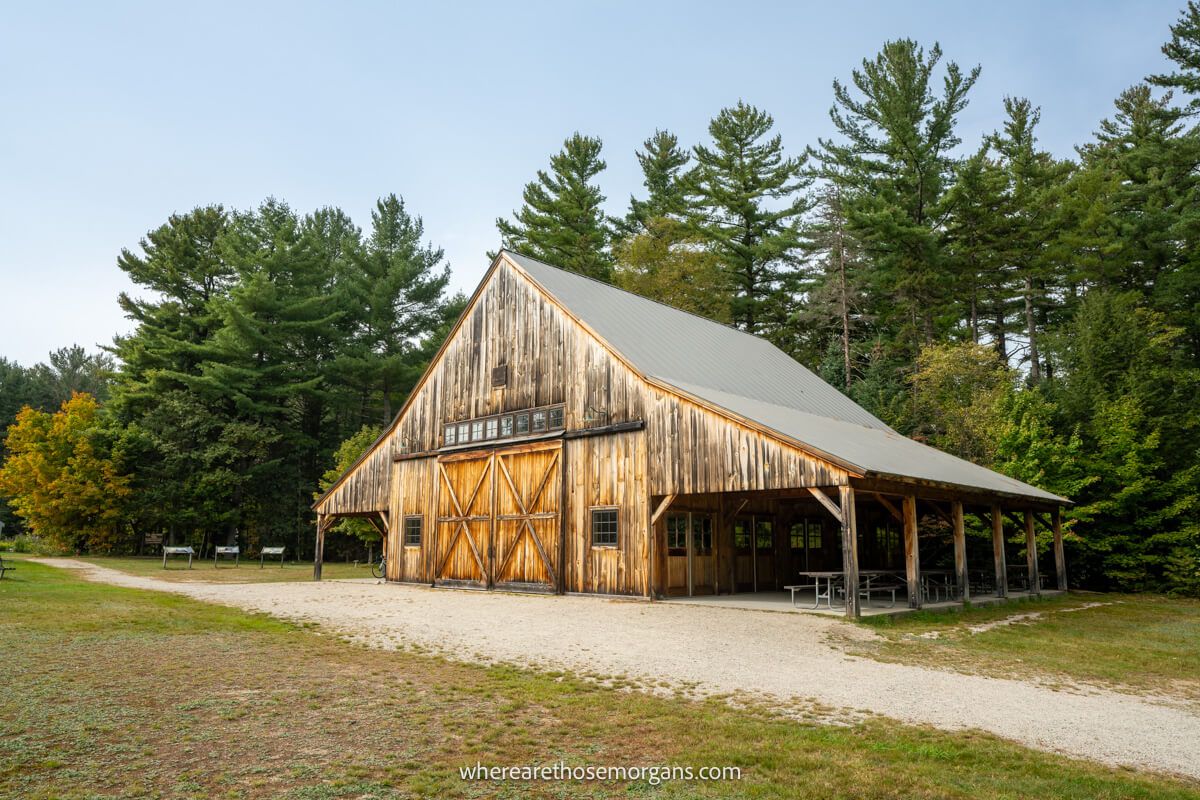 Large brown barn with sloping roof in front of evergreen trees