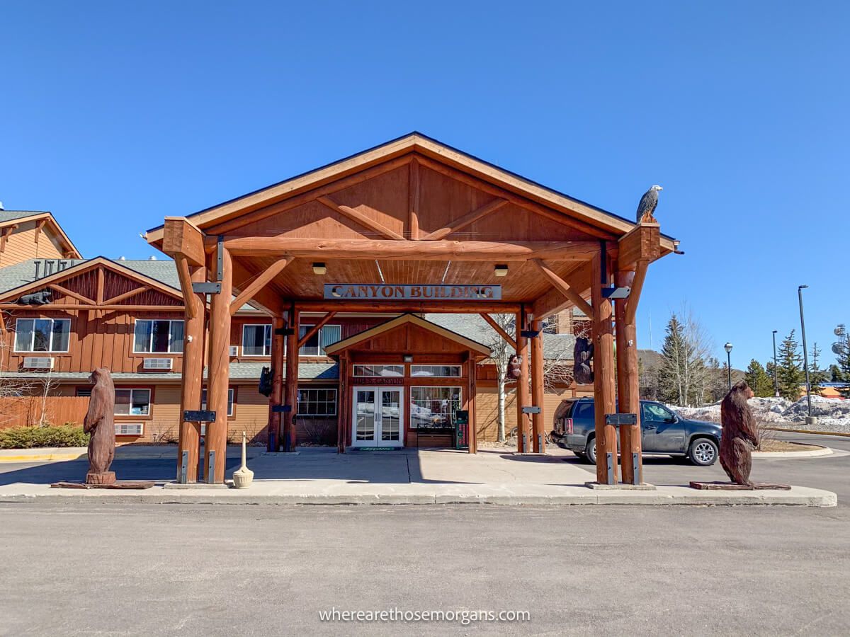 Exterior photo of a hotel near Yellowstone with huge wooden beams forming a porch underneath a brilliant blue sky