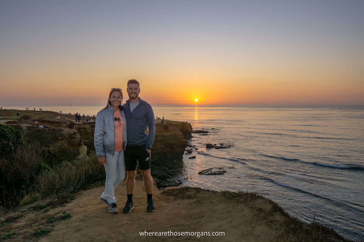 Man and woman posing for a photo with a sunset in the background along a San Diego beach