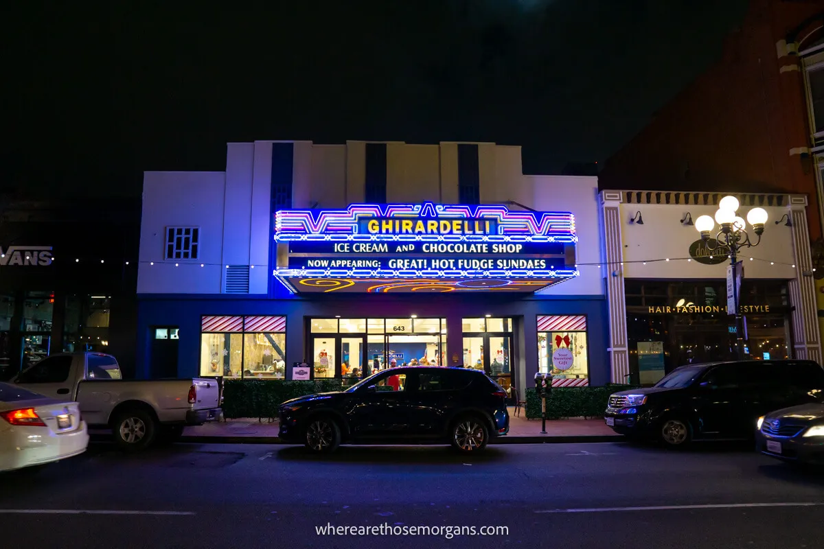 Photo of a road leading to parked cars and Ghirardelli's ice cream store lit up at night in the Gaslamp Quarter in San Diego