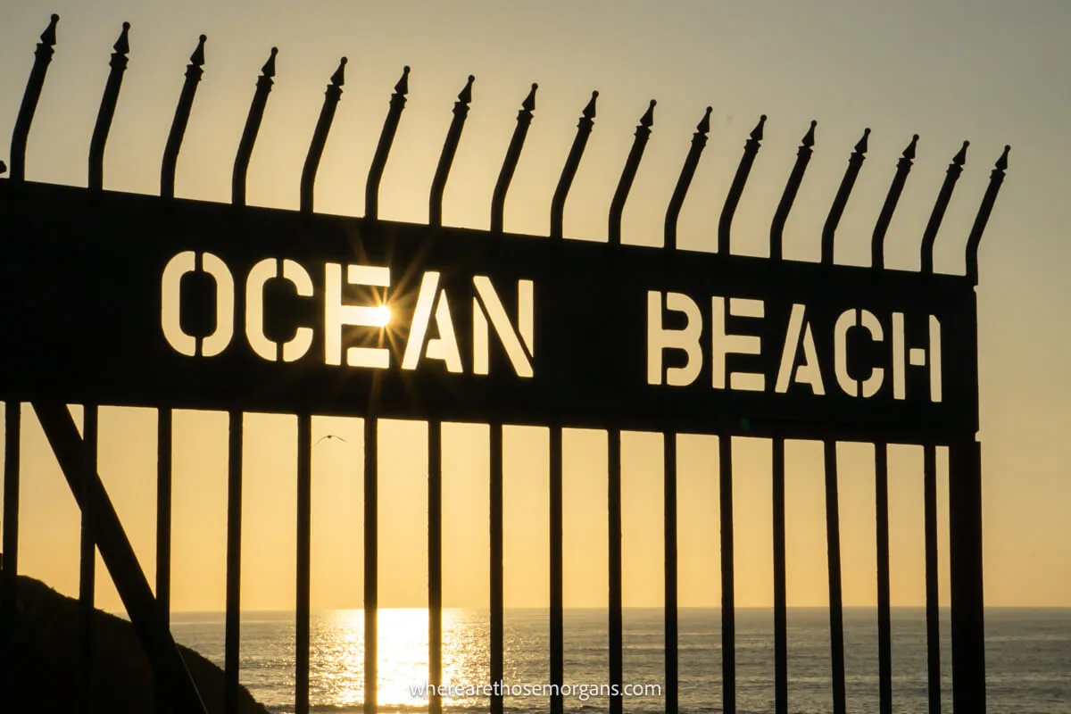 Gated fence looking at the ocean near sunset with the words Ocean Beach carved out and silhouetted