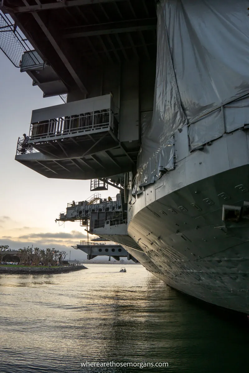 Photo taken at sea level of the underneath and back left side of a gigantic aircraft carrier called the USS Midway not long before sunset