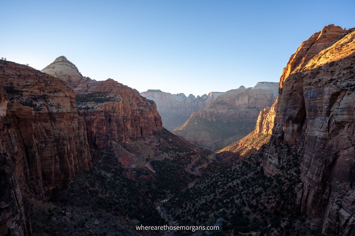 Tall red rock canyon walls flanking a deep valley as seen from an elevated rocky viewpoint at sunset with orange light glowing and no clouds in the sky at Zion Canyon Overlook