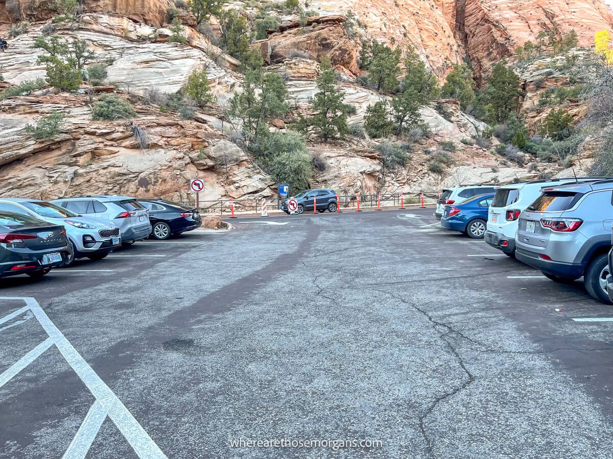 Photo of cars parked in a small lot and a trailhead in the distance leading up a rock face