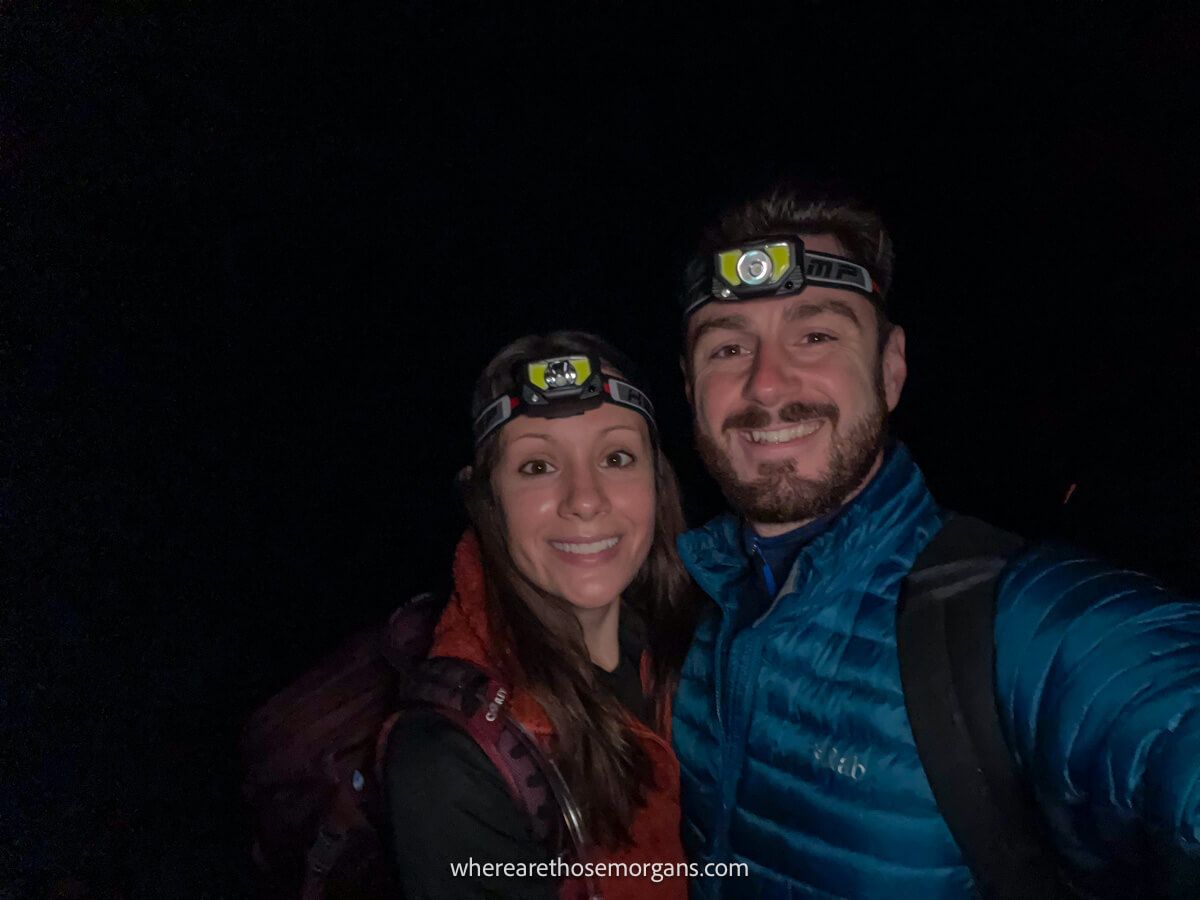 Photo a couple taking a selfie at night with coats, headlamps and backpacks on