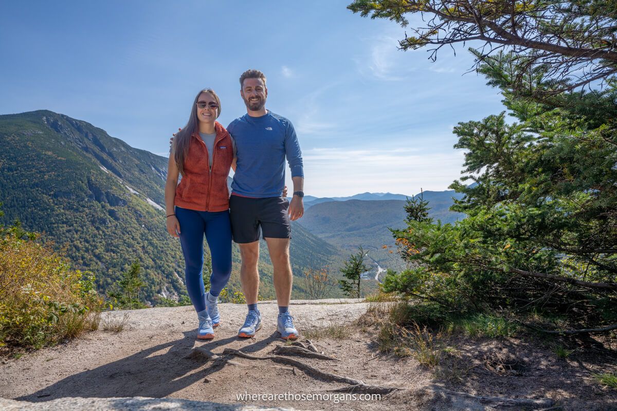 Photo of a couple at a hike summit overlooking a deep valley with hills and trees