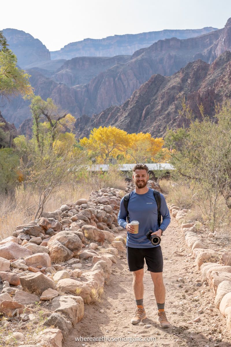 Photo of a hiker holding a camera and hot chocolate at the bottom of the grand canyon