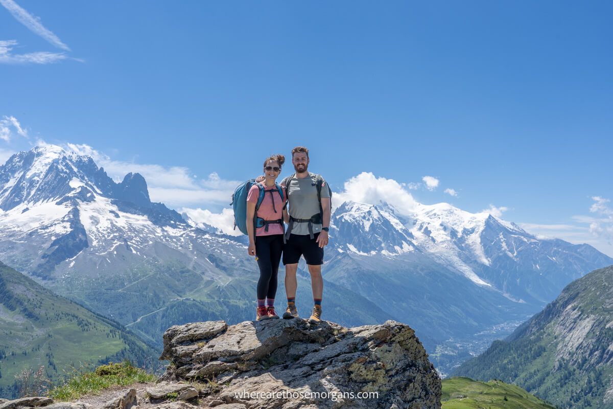 Photo of a couple standing together with backpacks on a hike and far reaching mountain views in the distance