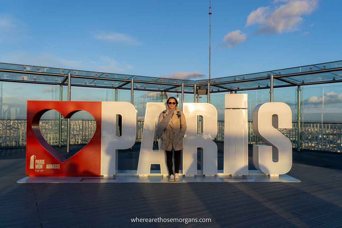 Photo of a tourist standing in front of a Paris sign on a rooftop