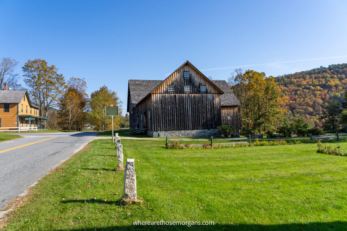 Old wooden building in rural Vermont with grass and hills covered in trees