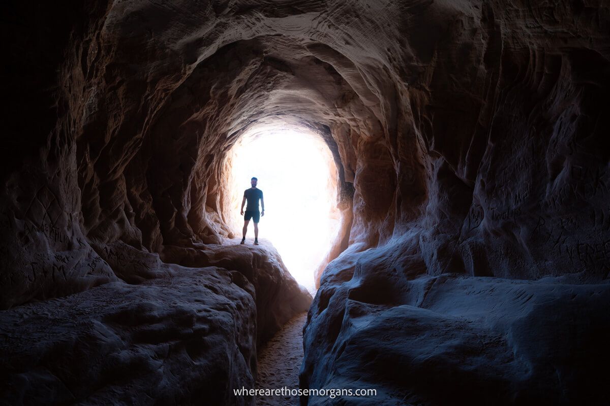 Hiker silhouetted against light at a small entrance to a tunnel