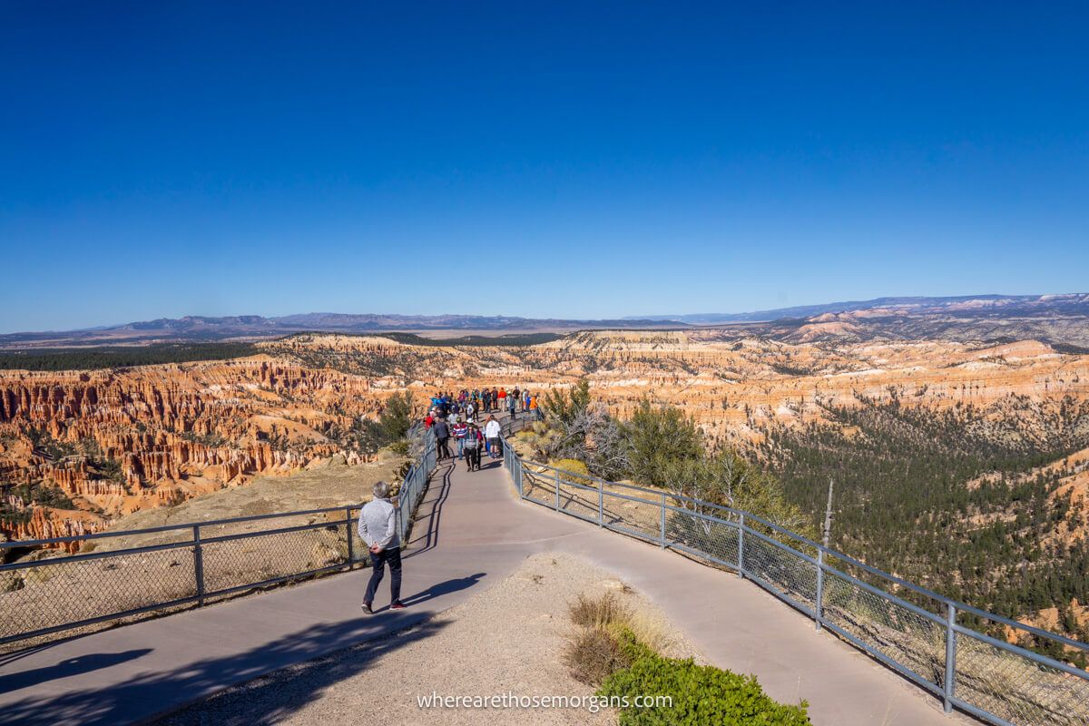 Pedestrian walkway filled with tourists leading to a viewpoint overlooking the unique Bryce Canyon sandstone landscape on a clear sunny day