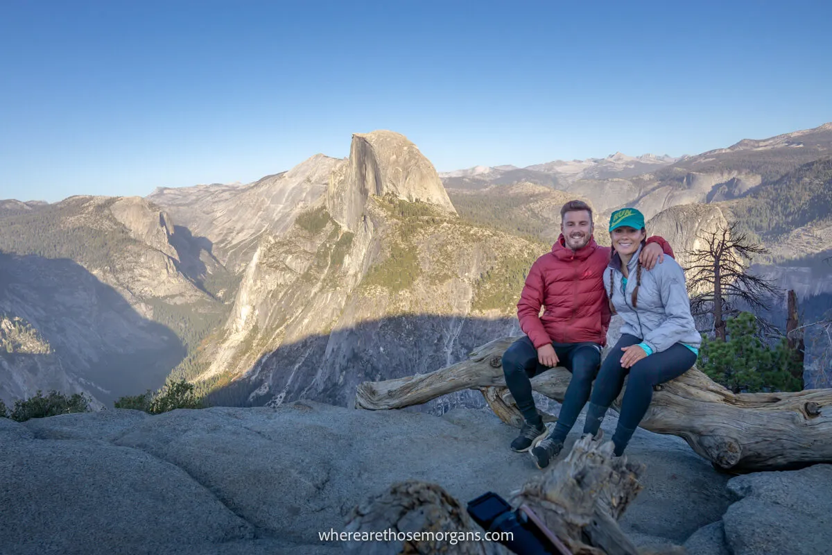 Photo of a couple sitting together on a log with views overlooking Half Dome in Yosemite National Park in the late afternoon with large shadows cast across the canyon below