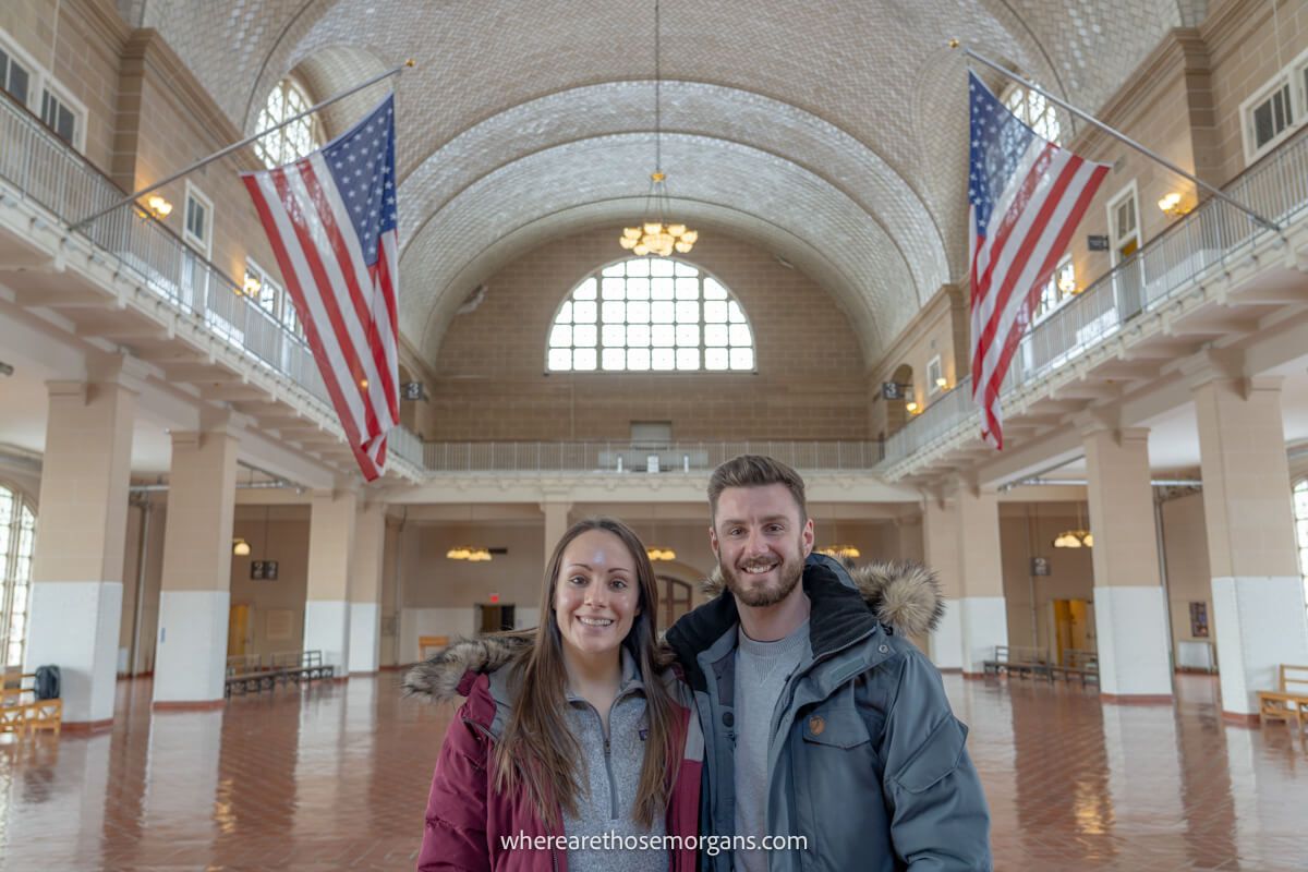 Photo of a couple inside Ellis Island Immigration Museum hall with American flags flying in a large room