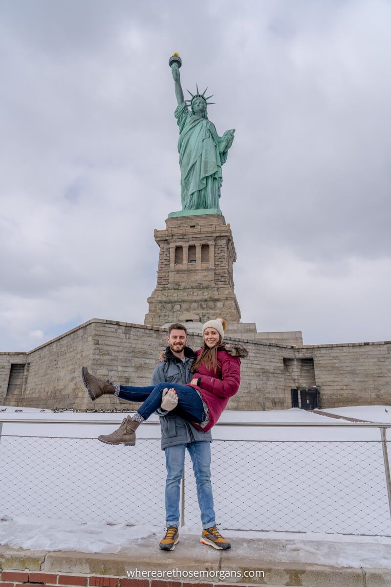 Photo of a couple in front of the Statue of Liberty with snow on the ground