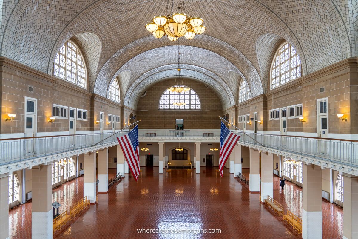 Photo of the inside of Ellis Island Immigration Museum from the second floor looking down at the arrivals hall with flags flying and light coming in