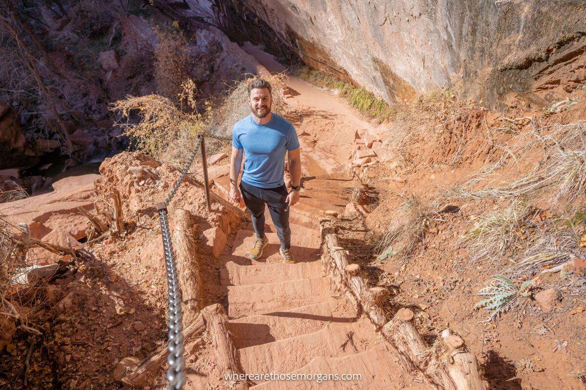Hiker in blue t-shirt on a stone staircase covered in red dust next to a metal rail in a red rock landscape