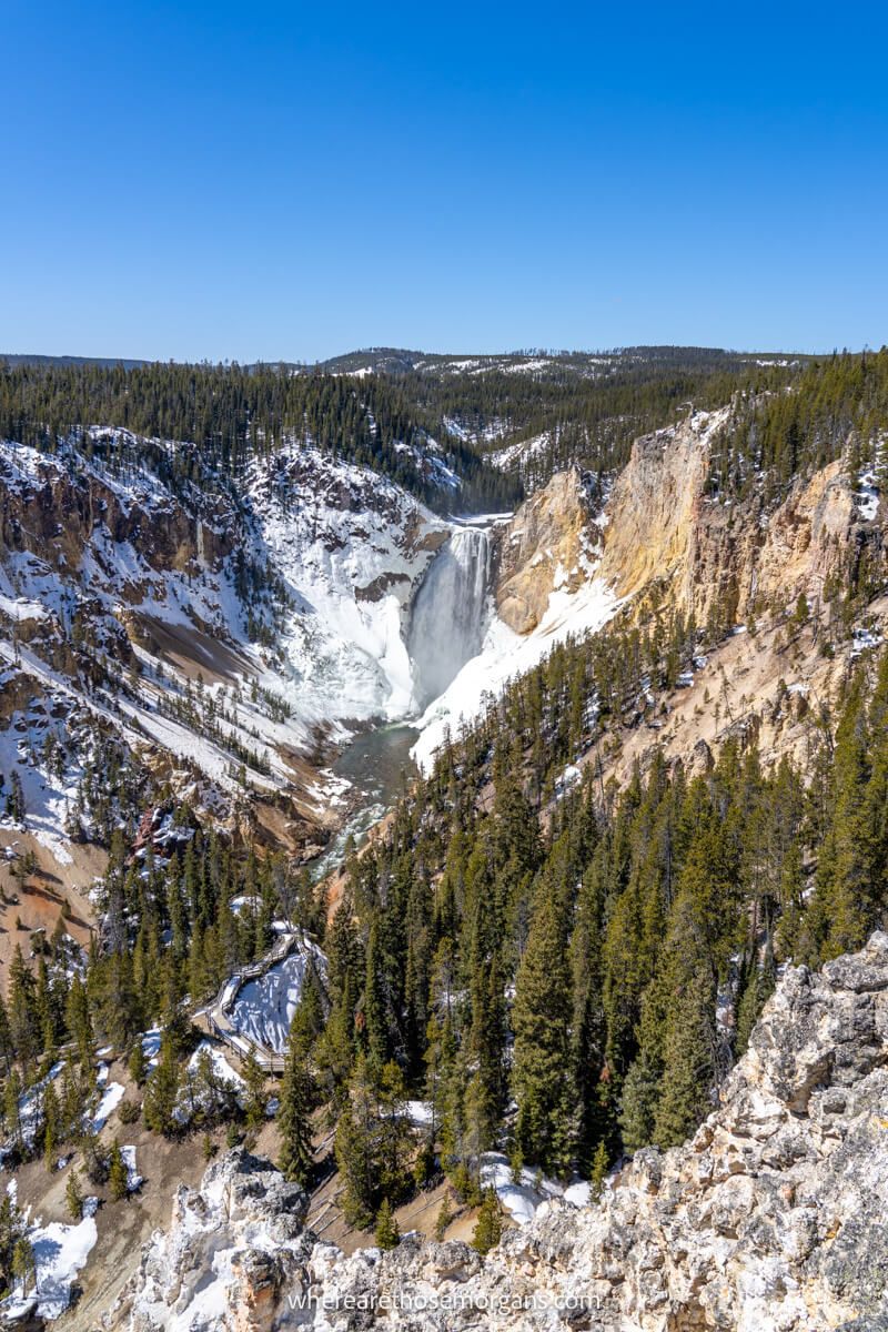 Photo of a deep V-shaped canyon covered in a light layer of snow with evergreen trees leading to a powerful waterfall dropping into the canyon on a sunny day
