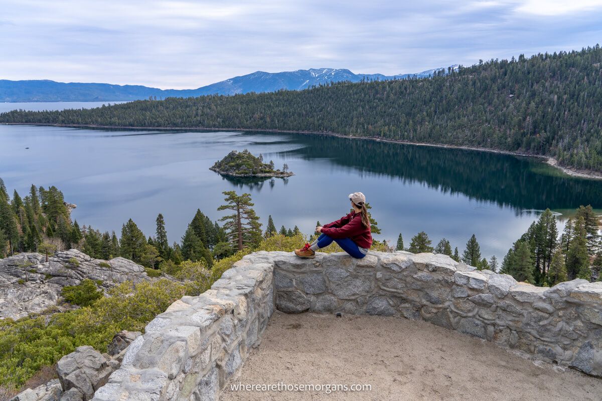 Hiker sat on a stone wall overlooking a bay with a small island in the middle and clouds in the sky
